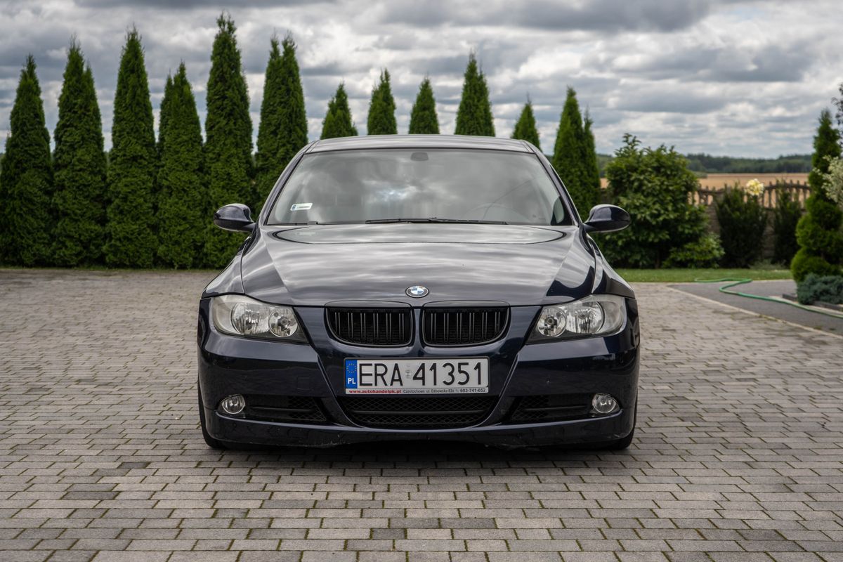 Ciemnoniebieskie BMW serii 3 E90 na kostce brukowej, polska tablica rejestracyjna