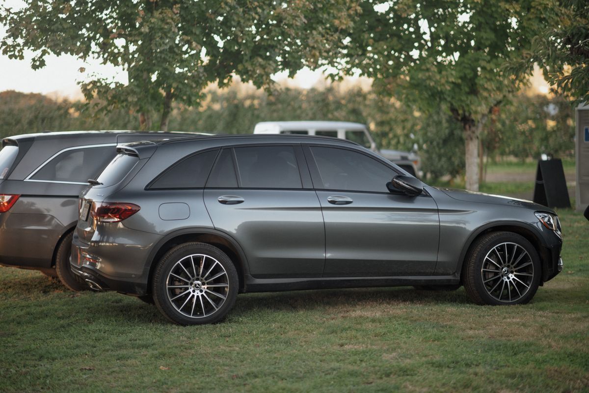 Szary Mercedes GLC w profilu, zaparkowany na trawie pod drzewami