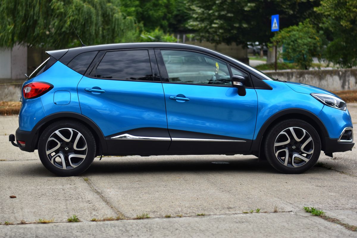 Niebieski Renault Captur w profilu, czarny dach, parking w świetle dnia