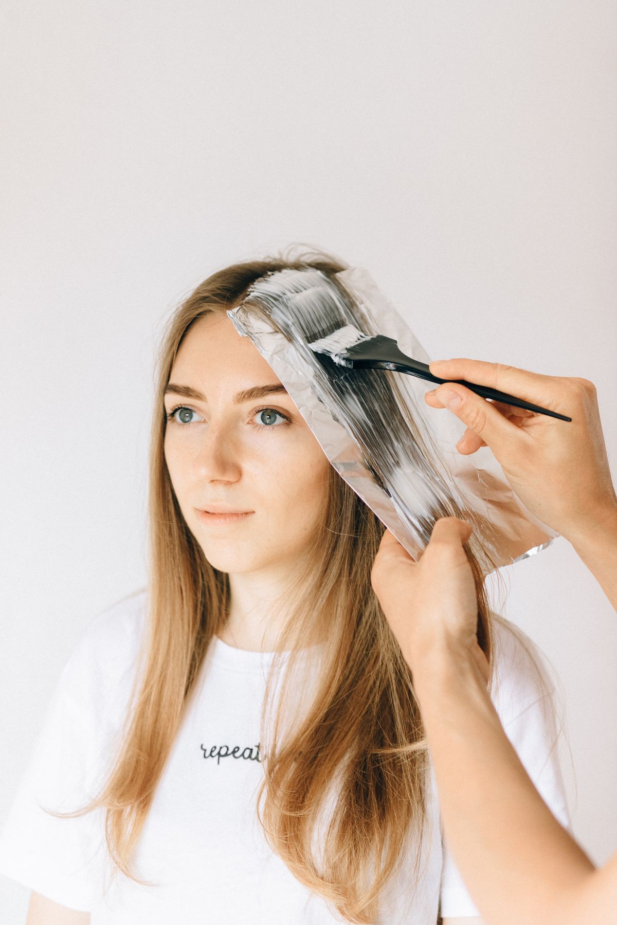 Stylistka nakłada rozjaśniacz na pasma owinięte folią — balayage w trakcie